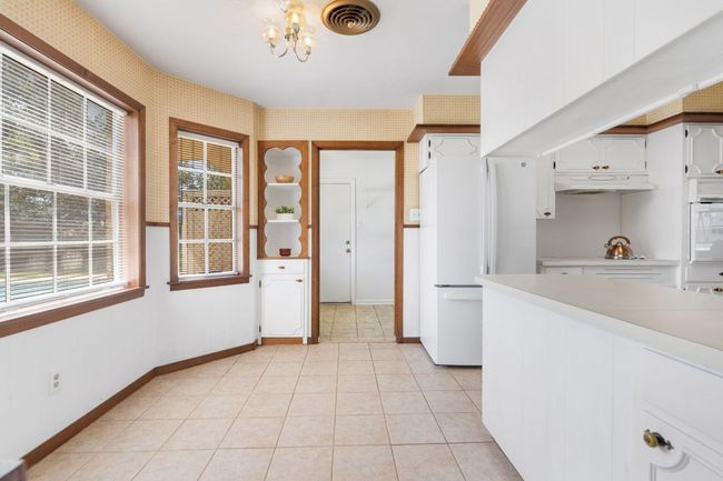 Kitchen featuring freestanding refrigerator, light countertops, a chandelier, wallpapered walls, and white cabinets. The doorway opens to the laundry room. | Image 11