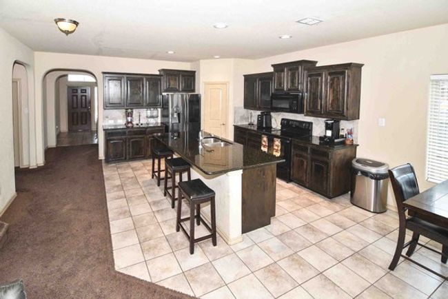 Kitchen featuring black appliances, a breakfast bar area, arched walkways, a sink, and light tile patterned floors | Image 13