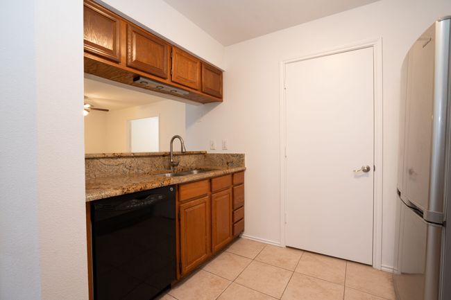 Kitchen with freestanding refrigerator, light tile patterned flooring, brown cabinetry, dishwasher, and a sink | Image 24