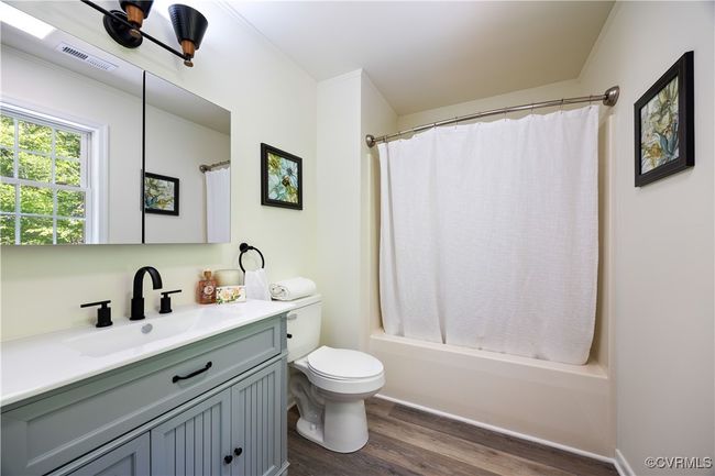 Full bathroom featuring wood finished floors, vanity, shower / tub combo with curtain, toilet, and visible vents | Image 25