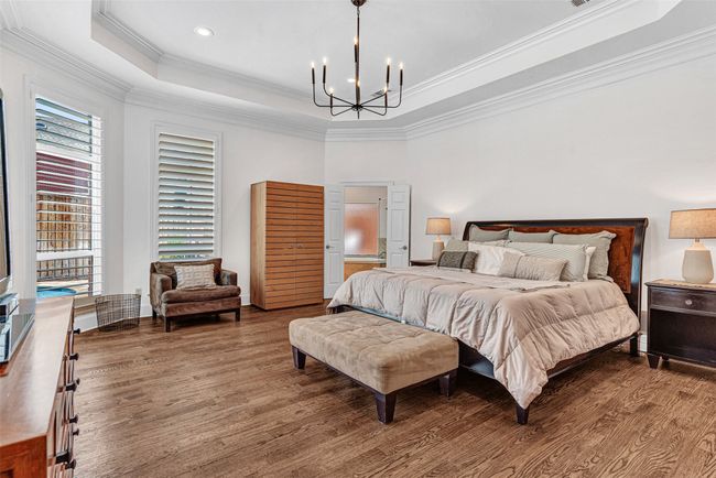 The primary suite is located off the family room for the ultimate in privacy, with wood floors, tray ceiling with crown molding and a bay windows offering pool and patio views through plantation shutters. | Image 10