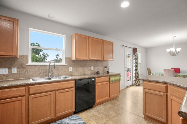 Kitchen featuring dishwasher, decorative backsplash, a chandelier, light floors, and hanging light fixtures | Image 7