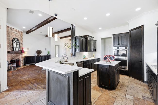 Kitchen featuring stone tile floors, stainless steel appliances, beam ceiling, a peninsula, and dark cabinetry | Image 14