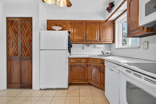 Kitchen with white appliances, brown cabinets, light countertops, light tile patterned floors, and crown molding | Image 6