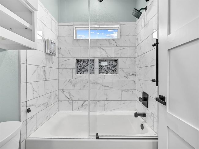 This stylish Jack & Jill bath features a quartz-top vanity with black hardware and a beautifully tiled tub/shower combo with built-in niches and frameless glass—perfectly positioned between the two custom bunk rooms for added convenience and comfort. | Image 24