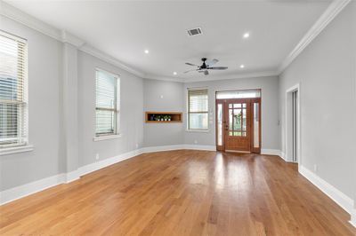 This is a spacious, well-lit room with polished hardwood floors, elegant crown molding, and multiple windows for natural light, a built-in shelf for electronic equipment. | Image 3