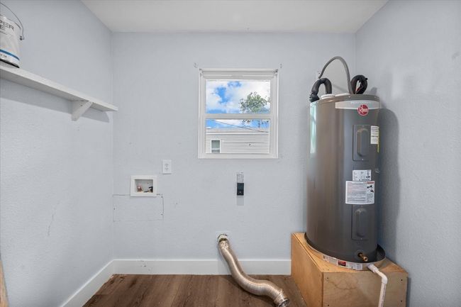 Washroom featuring electric water heater, washer hookup, dark wood-style floors, baseboards, and hookup for an electric dryer | Image 9