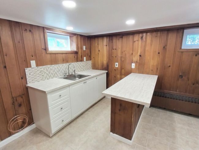 Kitchen with a sink, light countertops, white cabinets, a baseboard radiator, and wood walls | Image 28