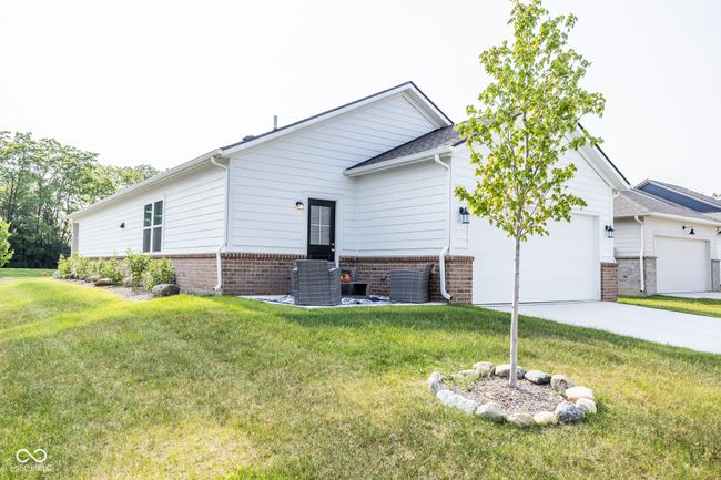 view of side of home with an attached garage, brick siding, a lawn, driveway, and central AC unit | Image 19