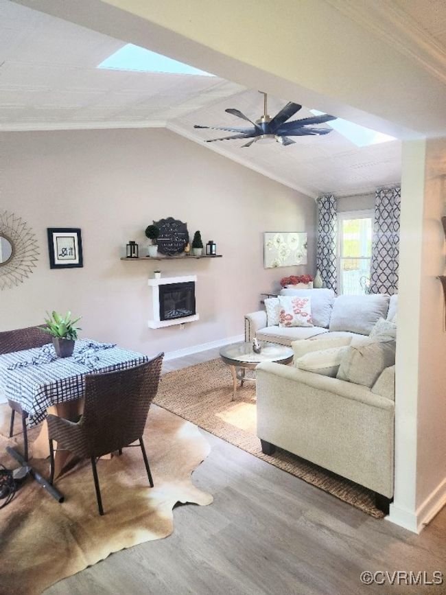 Living area with ceiling fan, a skylight, wood finished floors, a glass covered fireplace, and lofted ceiling | Image 9