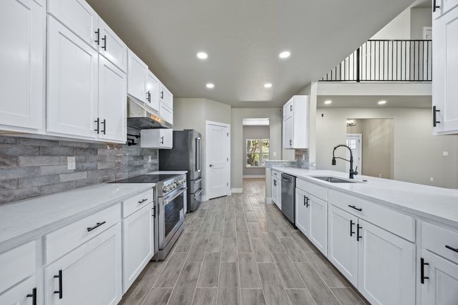 Kitchen featuring tasteful backsplash, white cabinets, a sink, under cabinet range hood, and stainless steel appliances | Image 7