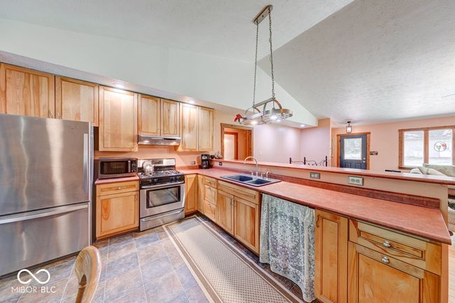 kitchen featuring appliances with stainless steel finishes, under cabinet range hood, a peninsula, vaulted ceiling, and light brown cabinets | Image 42