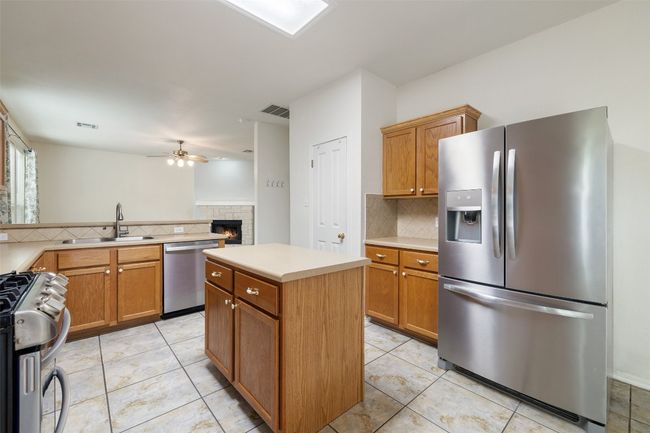 Kitchen featuring appliances with stainless steel finishes, a sink, a fireplace, a ceiling fan, and decorative backsplash | Image 11