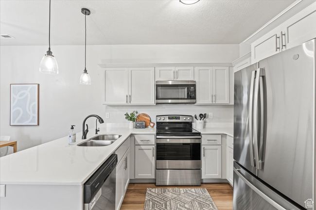 Kitchen with stainless steel appliances, a peninsula, hanging light fixtures, light wood-type flooring, and light stone countertops | Image 15