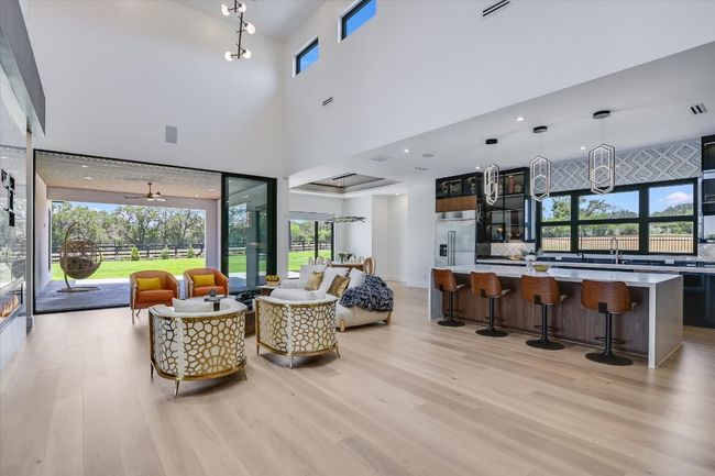 Living room with light wood floors and a towering ceiling, fireplace and doors that open up along the back of the house/patio | Image 11