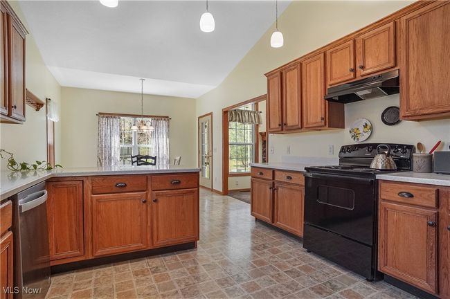 Kitchen with black electric range oven, dishwasher, under cabinet range hood, and brown cabinets | Image 22