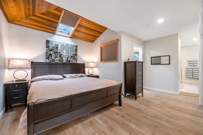 Bedroom featuring lofted ceiling with skylight, wood ceiling, light wood-style floors, and baseboards | Image 13