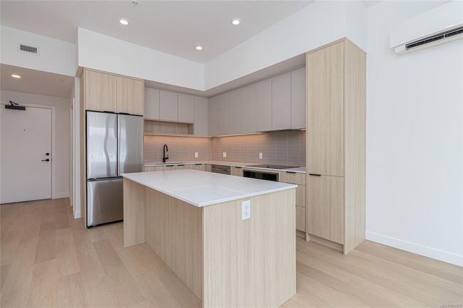 Kitchen featuring modern cabinets, stainless steel refrigerator, a wall unit AC, and a center island | Image 10