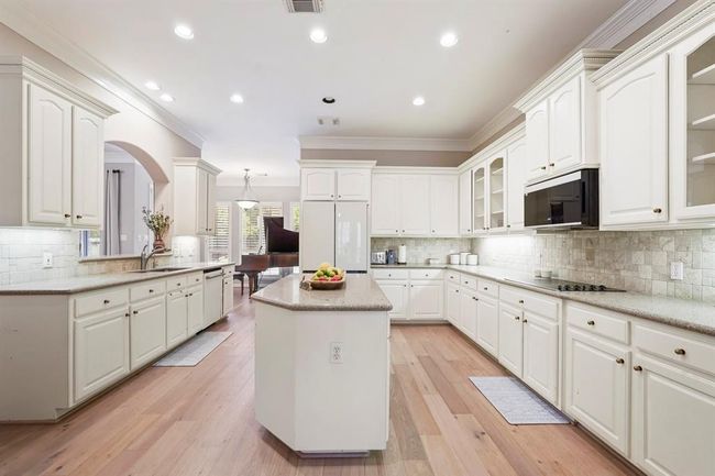Spacious kitchen with white cabinetry, granite countertops, and hardwood floors. Features an island, built-in appliances, and recessed lighting. | Image 9