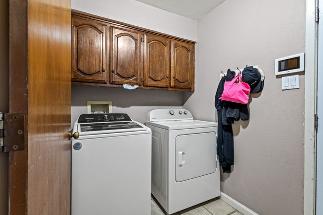 Washroom featuring cabinet space, washing machine and clothes dryer, and light tile patterned flooring | Image 24
