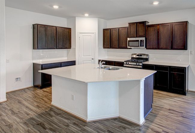Kitchen featuring appliances with stainless steel finishes, a sink, tasteful backsplash, wood finished floors, and a kitchen island with sink | Image 8