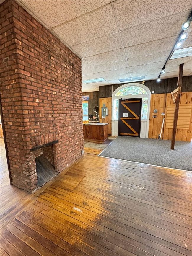Unfurnished living room featuring a paneled ceiling, brick wall, hardwood / wood-style flooring, and wood walls | Image 7