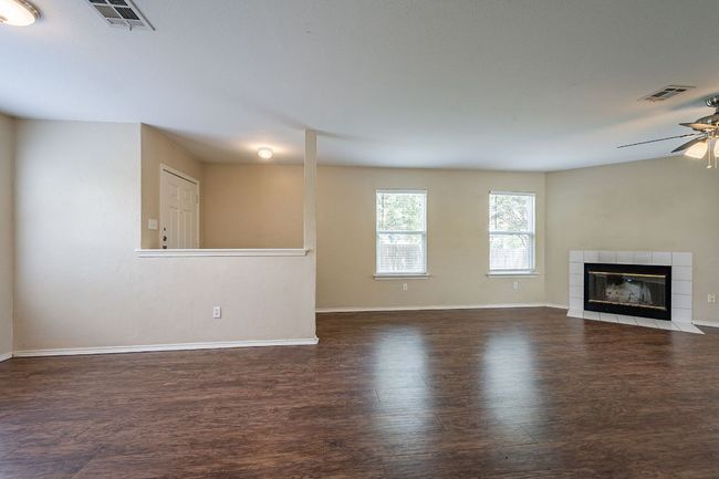 Unfurnished living room with ceiling fan, wood finished floors, baseboards, and a tiled fireplace | Image 6