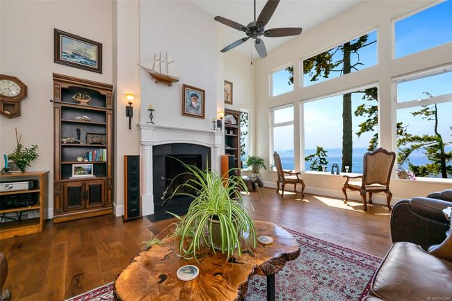 Living room featuring a towering ceiling, wood finished floors, a fireplace with flush hearth, and ceiling fan | Image 38