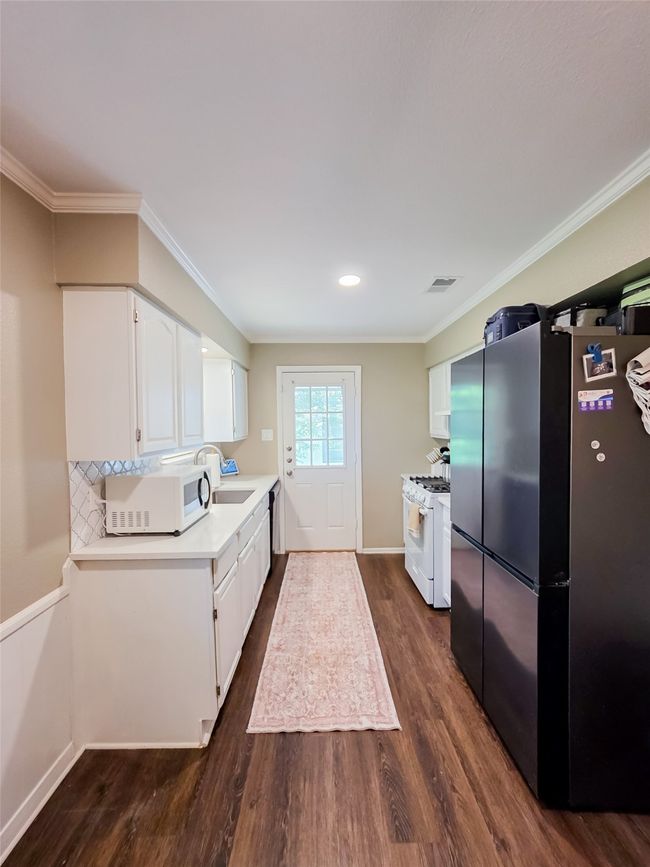 Kitchen with white appliances, dark wood-style floors, a sink, white cabinetry, and ornamental molding | Image 23