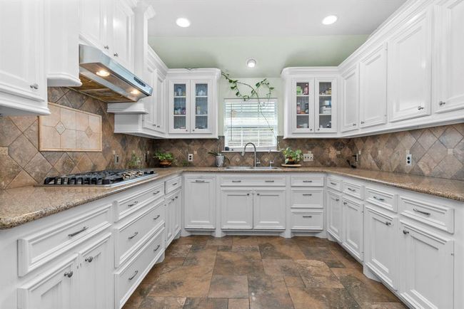 This is a spacious kitchen featuring white cabinetry, granite countertops, a gas cooktop, and tile flooring. There's ample storage and natural light coming through the windows. | Image 22