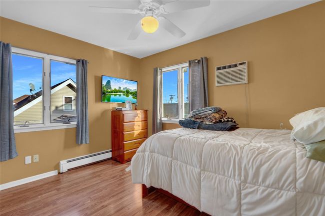 Bedroom featuring baseboard heating, an AC wall unit, multiple windows, and hardwood / wood-style floors | Image 24