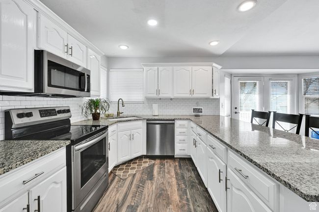 Kitchen with white cabinets, a peninsula, dark wood finished floors, appliances with stainless steel finishes, and a sink | Image 15