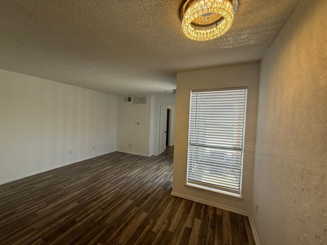Unfurnished room featuring dark wood-type flooring, a textured ceiling, a textured wall, and a chandelier | Image 5