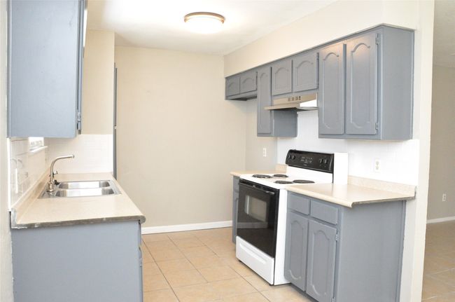 Kitchen with tasteful backsplash, gray cabinets, electric range, under cabinet range hood, and a sink | Image 13