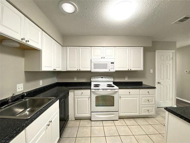 8836 Kitchen featuring white appliances, light tile flooring, a textured ceiling, white cabinetry, and sink | Image 16