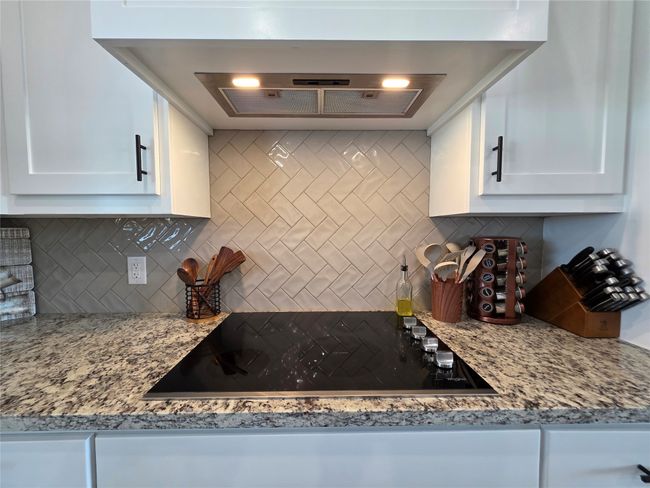 Kitchen featuring ventilation hood, black electric cooktop, decorative backsplash, and white cabinets | Image 12