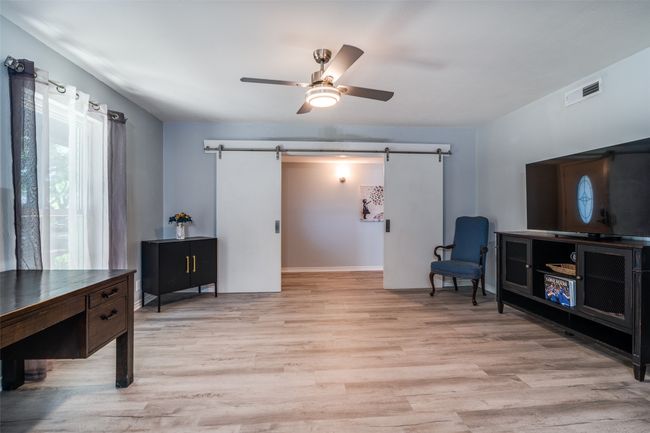 Living area featuring a barn door, light wood-style flooring, a ceiling fan, and baseboards | Image 9