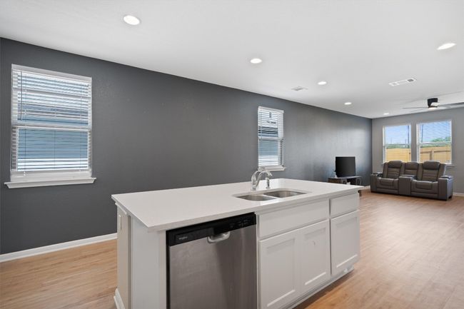 Kitchen with dishwasher, light wood-type flooring, white cabinets, an island with sink, and light countertops | Image 7