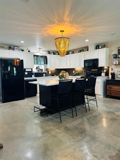 Kitchen with black appliances, a kitchen island, hanging light fixtures, white cabinets, and a breakfast bar | Image 3