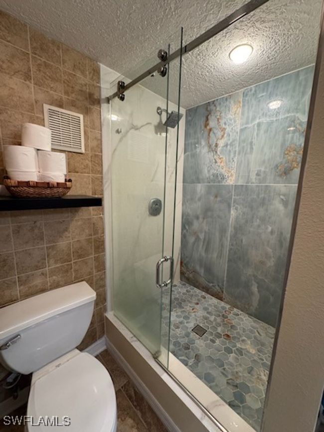Full bath featuring tile walls, a textured ceiling, toilet, and a shower stall | Image 14