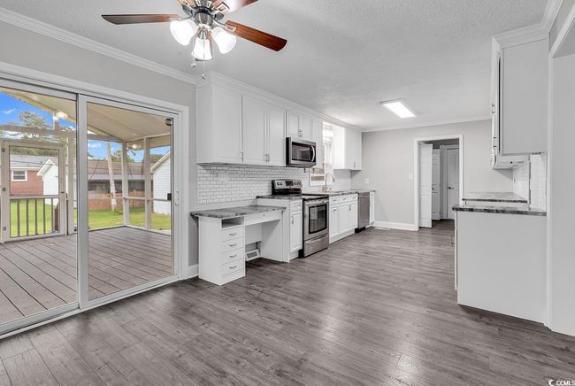 Kitchen with appliances with stainless steel finishes, decorative backsplash, white cabinets, a ceiling fan, and dark wood-style flooring | Image 9