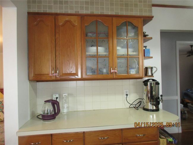 Kitchen with brown cabinets, glass insert cabinets, light countertops, and decorative backsplash | Image 4