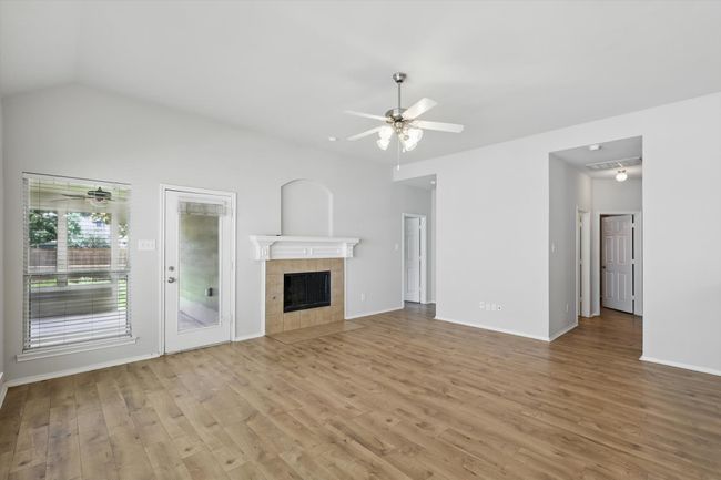 Unfurnished living room featuring ceiling fan, light wood finished floors, a fireplace, and vaulted ceiling | Image 14