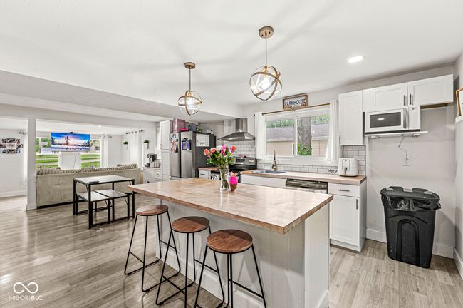 kitchen with appliances with stainless steel finishes, wall chimney range hood, light wood-style flooring, a breakfast bar, and white cabinets | Image 11