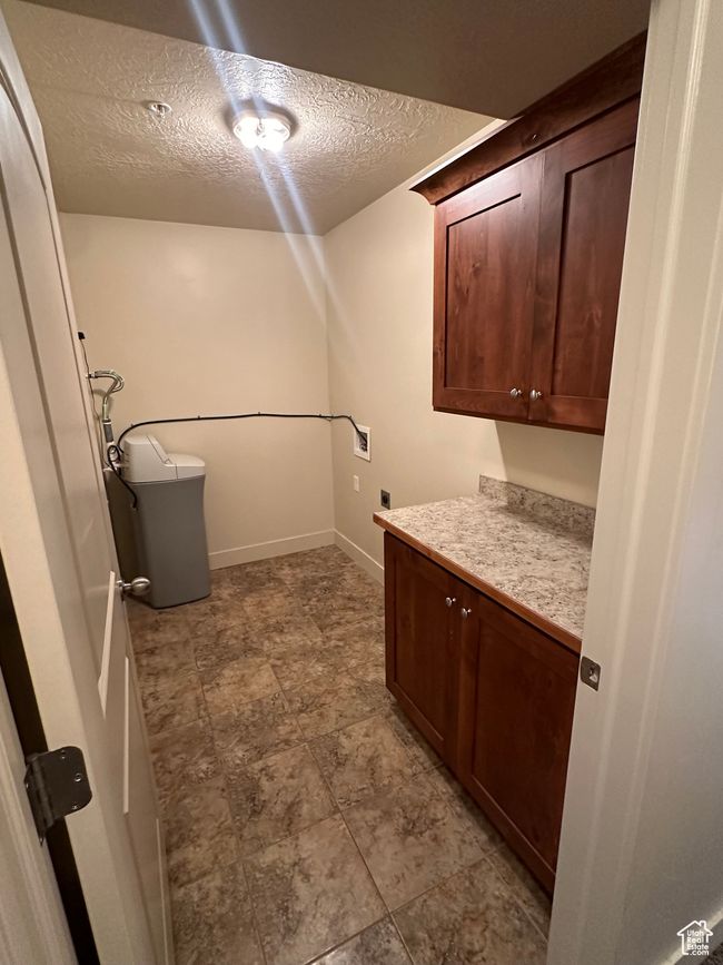 Washroom with a textured ceiling, hookup for an electric dryer, washer hookup, baseboards, and cabinet space | Image 11