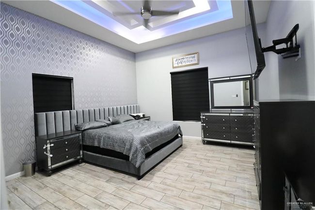 Bedroom with wallpapered walls, light wood-style flooring, a raised ceiling, baseboards, and a ceiling fan | Image 8