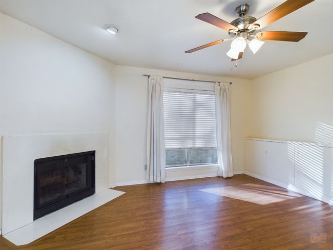 Unfurnished living room with ceiling fan, baseboards, wood finished floors, and a fireplace | Image 6
