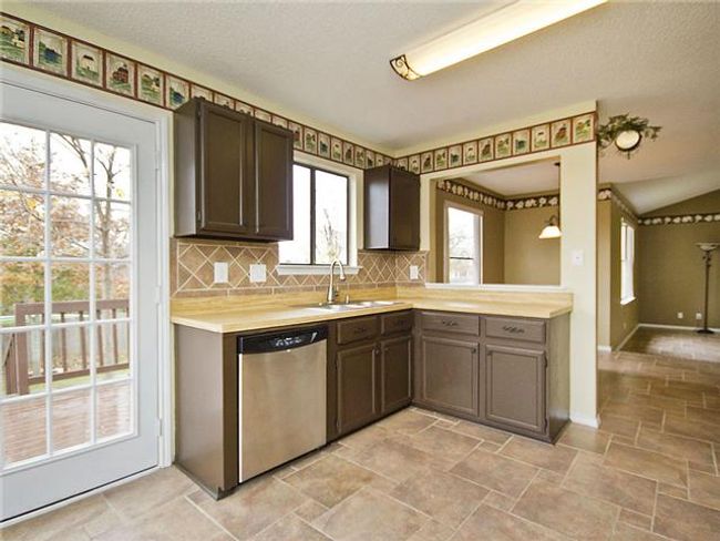 Kitchen featuring tasteful backsplash, light countertops, stone finish flooring, dishwasher, and a sink | Image 7
