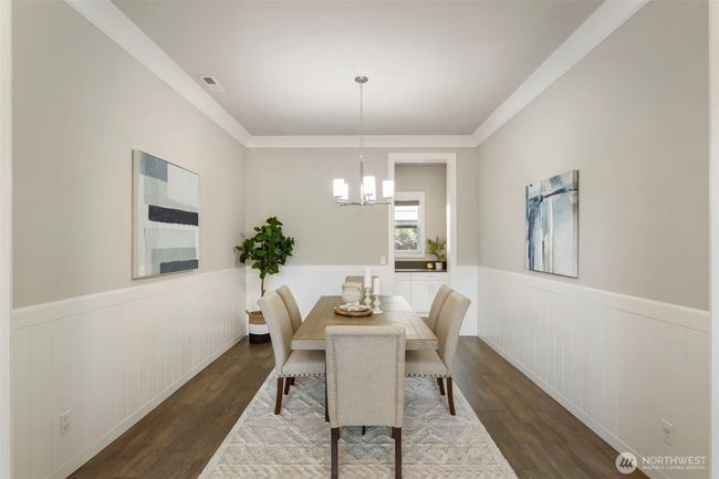 This elegant formal dining room features crisp wainscoting, warm hardwood floors, and a modern light fixture, creating a refined space for entertaining. A convenient pass-through leads to the drop zone, adding both function and flow to this thoughtfully designed layout. | Image 19