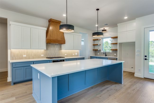 Kitchen featuring light wood-style flooring, a center island, premium range hood, open shelves, and a sink | Image 9